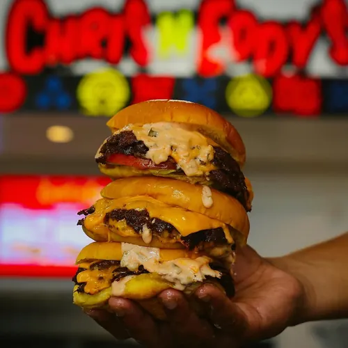 Three Chris N Eddy’s sliders in hand with the shop neon glowing behind